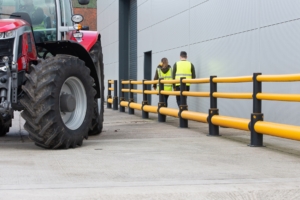 pedestrians walking down a walkway with barriers as tractor passes 