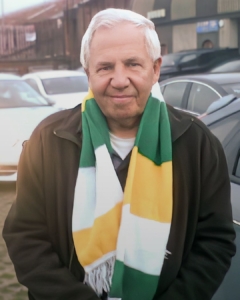 Uncle Robert, standing outside a football stadium, wearing a white, yellow and green striped football scarf