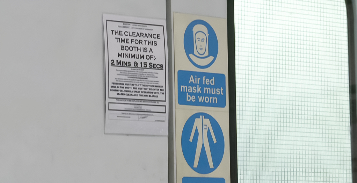 Signage on the entrance of a spray booth showing mist clearance times and that air-fed masks must be worn