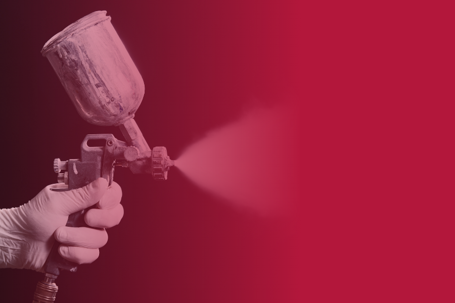 A gloved hand spraying paint from a spray gun connected to an air hose