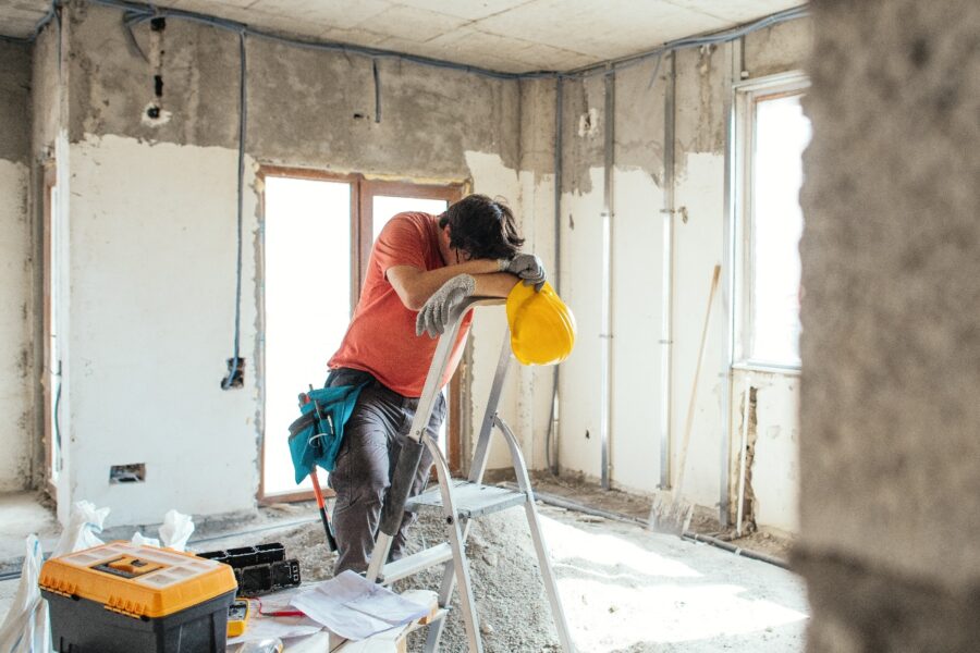 Tradesperson leaning head on ladder in room undergoing renovation